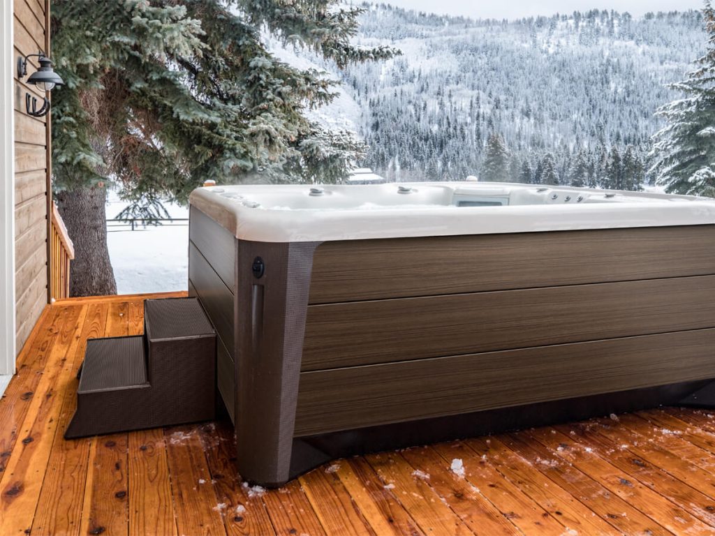 Hot tub on a snowy deck next to the house with steps for safe winter access