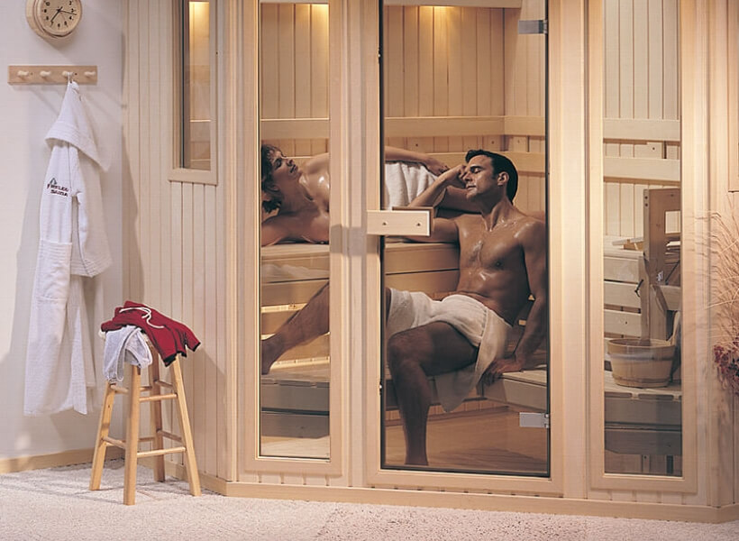 Man and woman sweating inside of a traditional sauna with chair and robe outside of sauna