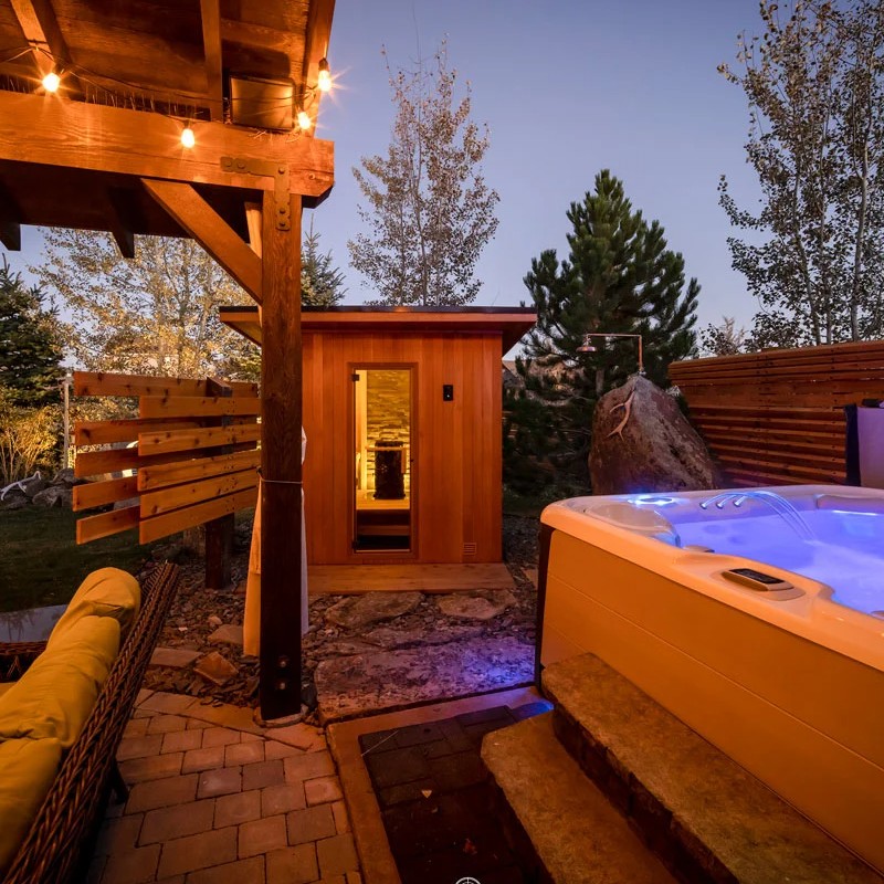 Small outdoor sauna next to a Hot Spring Spa in lit up backyard