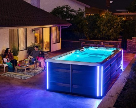 Endless Pools Swim Spa lit up in dark backyard with family sitting in outdoor furniture